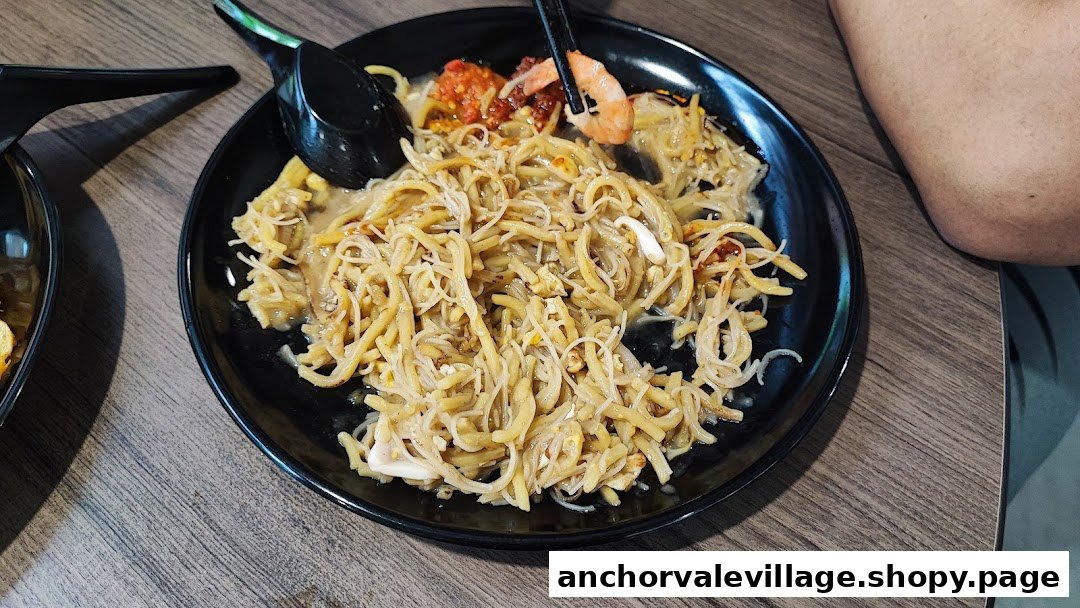 A close-up of a plate of Hokkien Mee with shrimp and chili on a wooden table.