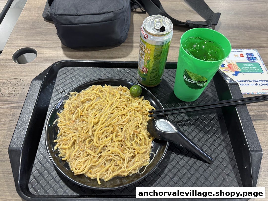 A plate of Hokkien Mee with a lime, chopsticks, and drinks on a tray.