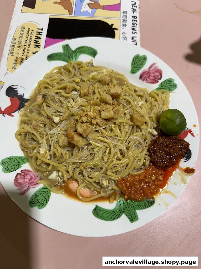 A delicious plate of Hokkien Mee with crispy pork lard, lime, and chili on a classic rooster plate.