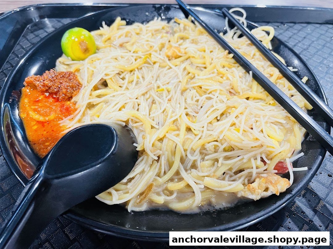 A close-up of a plate of Hokkien Mee with chili paste and a calamansi lime.