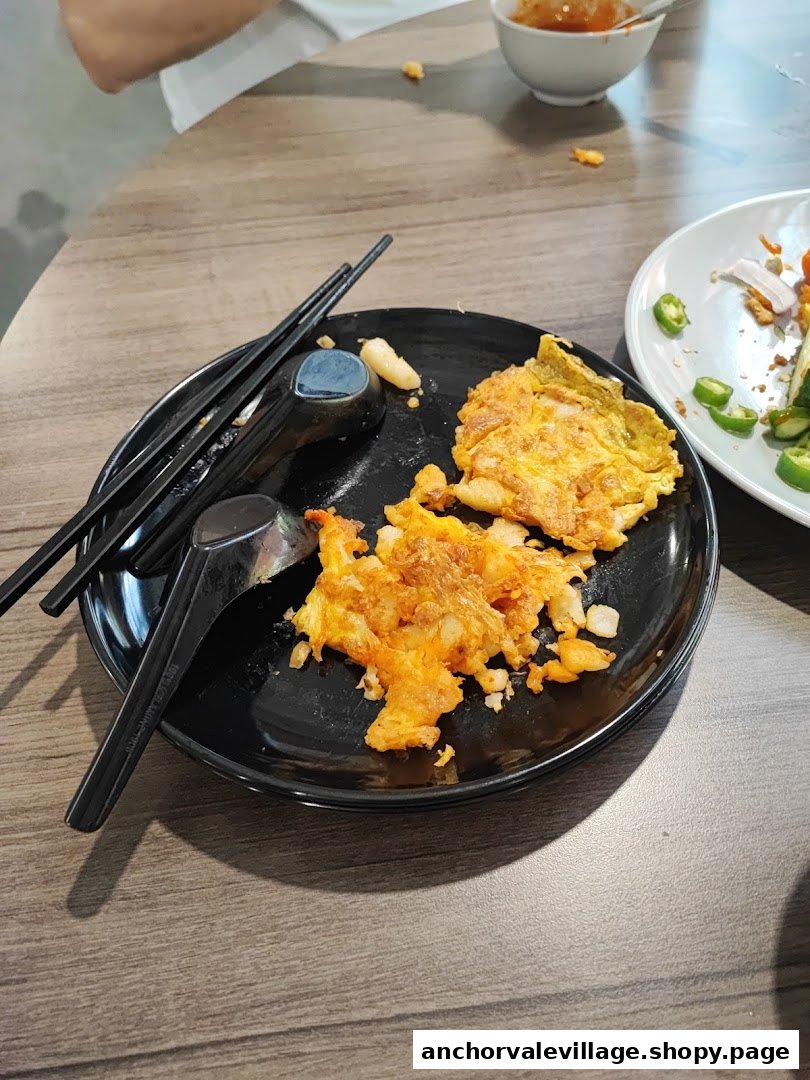 A plate of partially eaten fried oyster omelette with chopsticks and spoons on a wooden table.