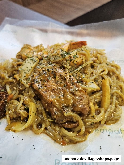 A close-up of a savory noodle dish with meat, seafood, and herbs from Rempah by Chilli Padi.
