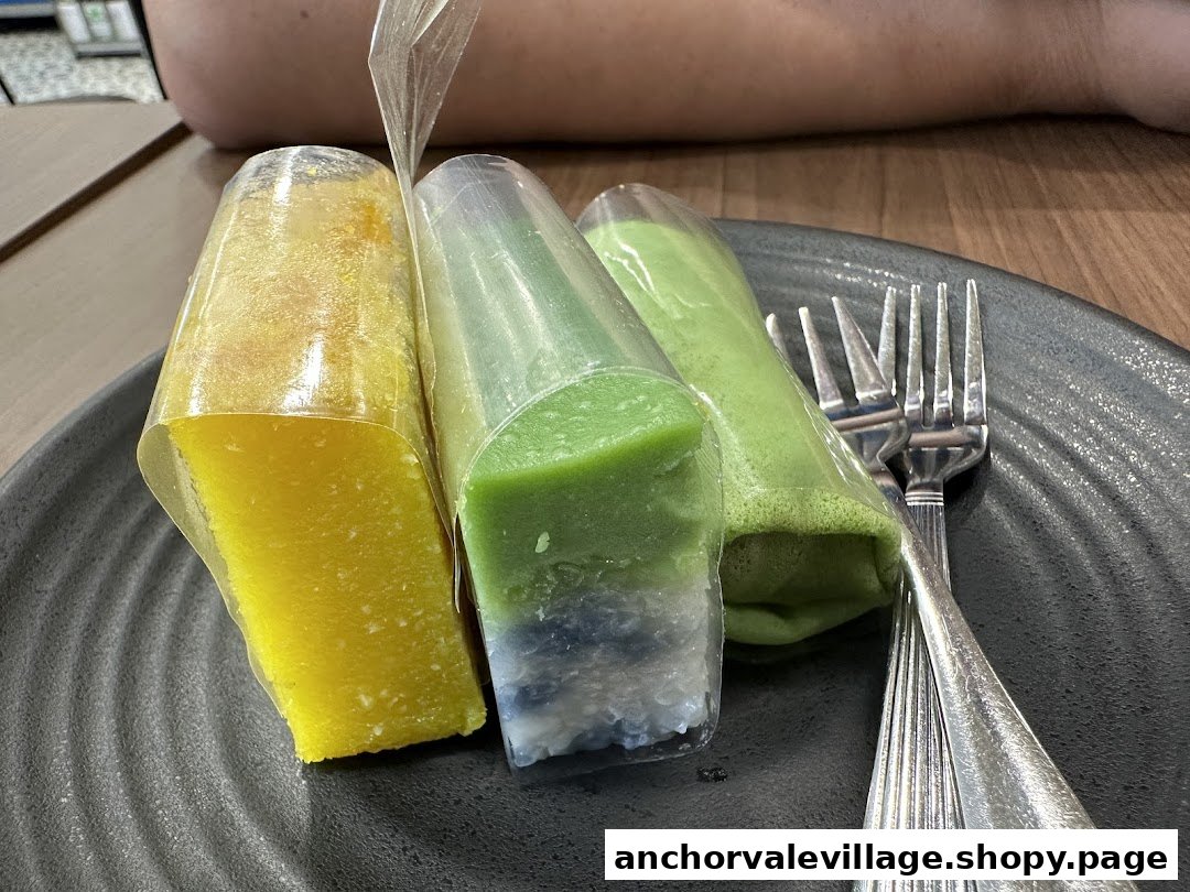 Three colorful traditional desserts, possibly kueh, served on a dark plate with a fork.