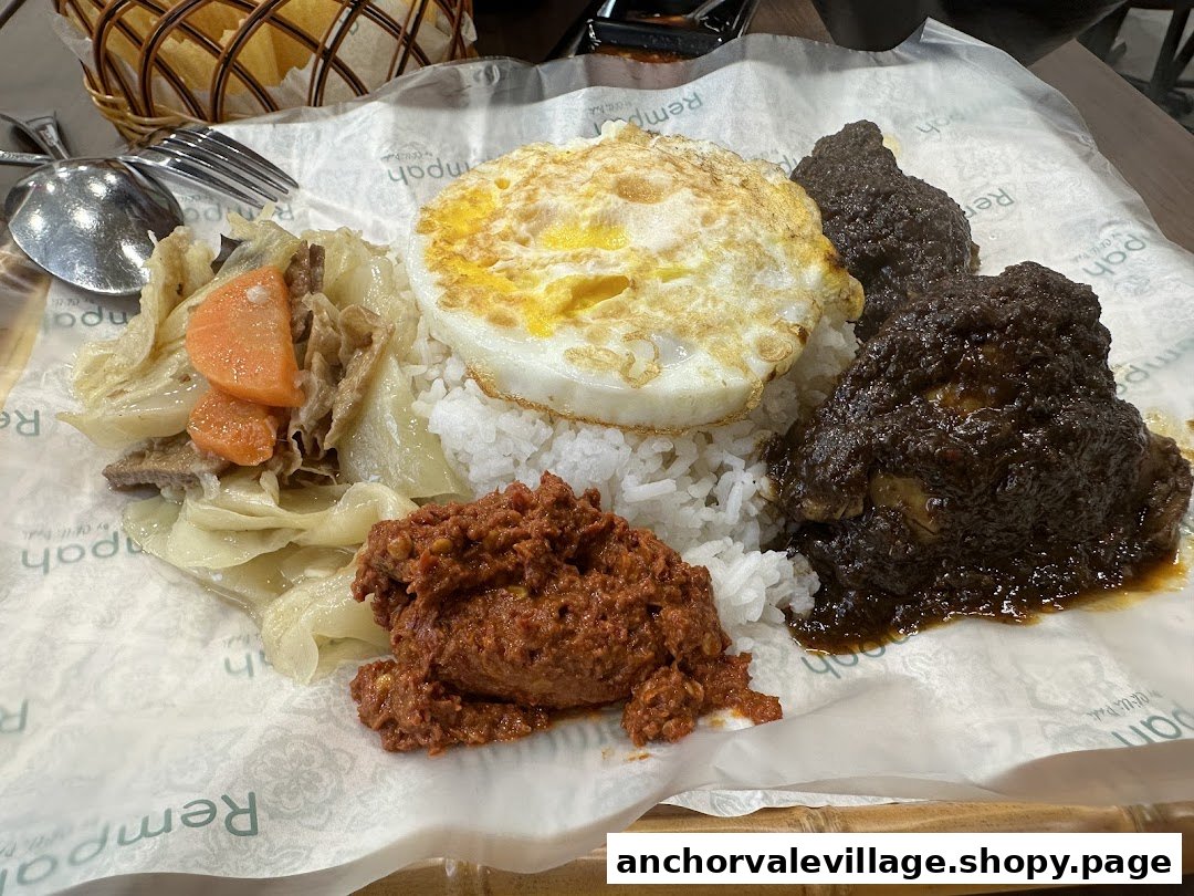A close-up of a delicious rice dish with fried egg, stewed vegetables, and rich meat rendang served on branded paper.