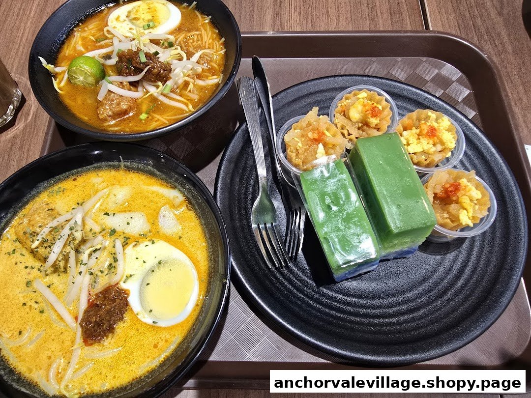 Two bowls of traditional noodles and assorted kueh desserts on a tray.