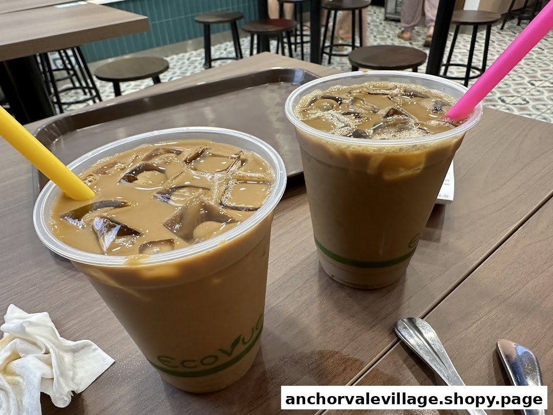 Two refreshing iced coffee drinks with colorful straws on a wooden table inside the shop.