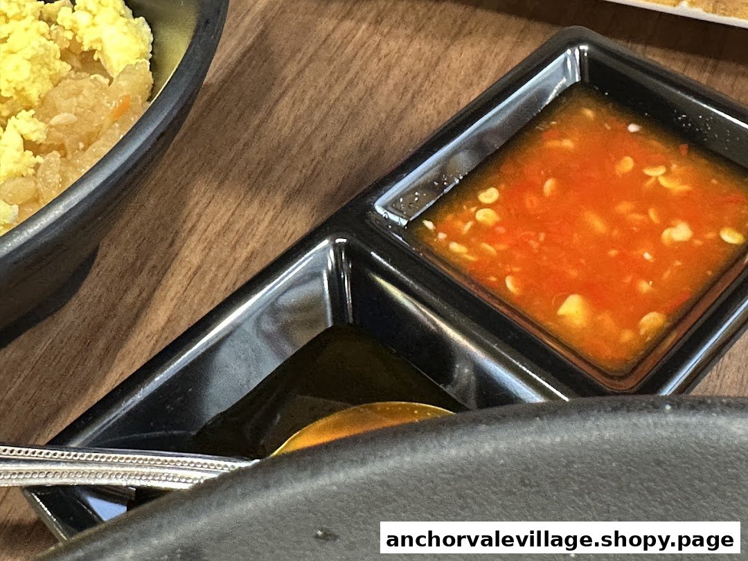 Close-up of two dipping sauces and a side dish, likely rice, on a wooden table.