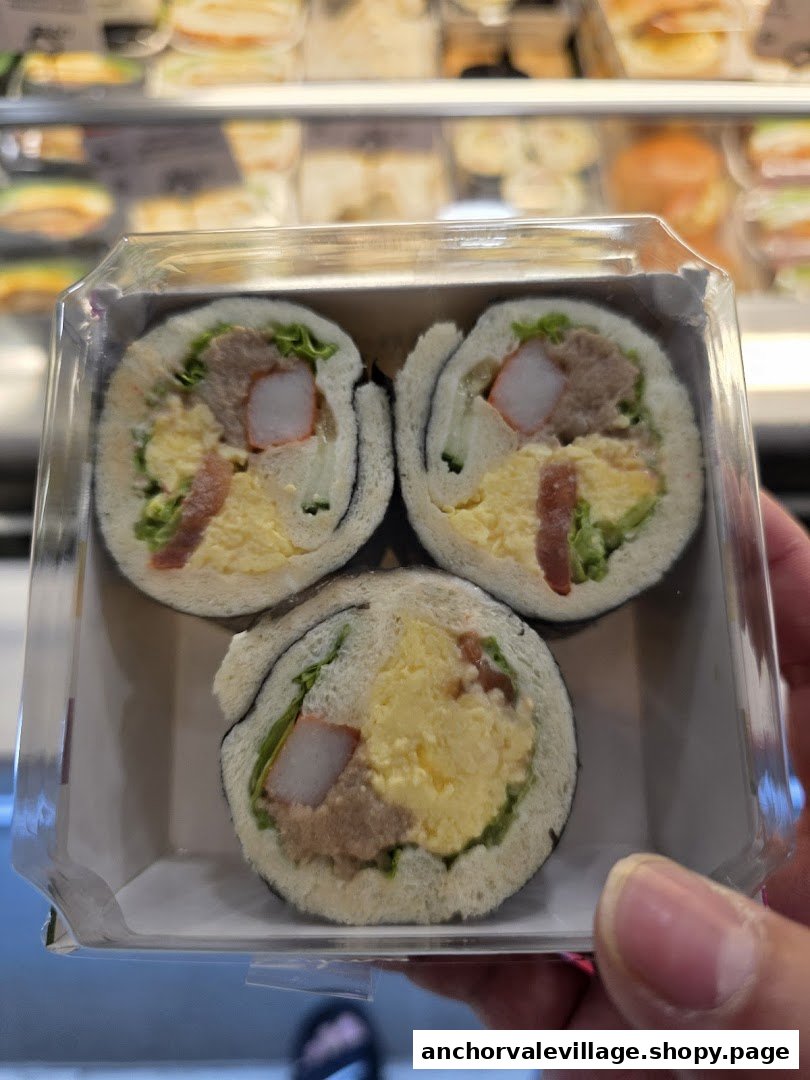 Three unique sandwich rolls with various fillings in a clear plastic container, held by a hand.