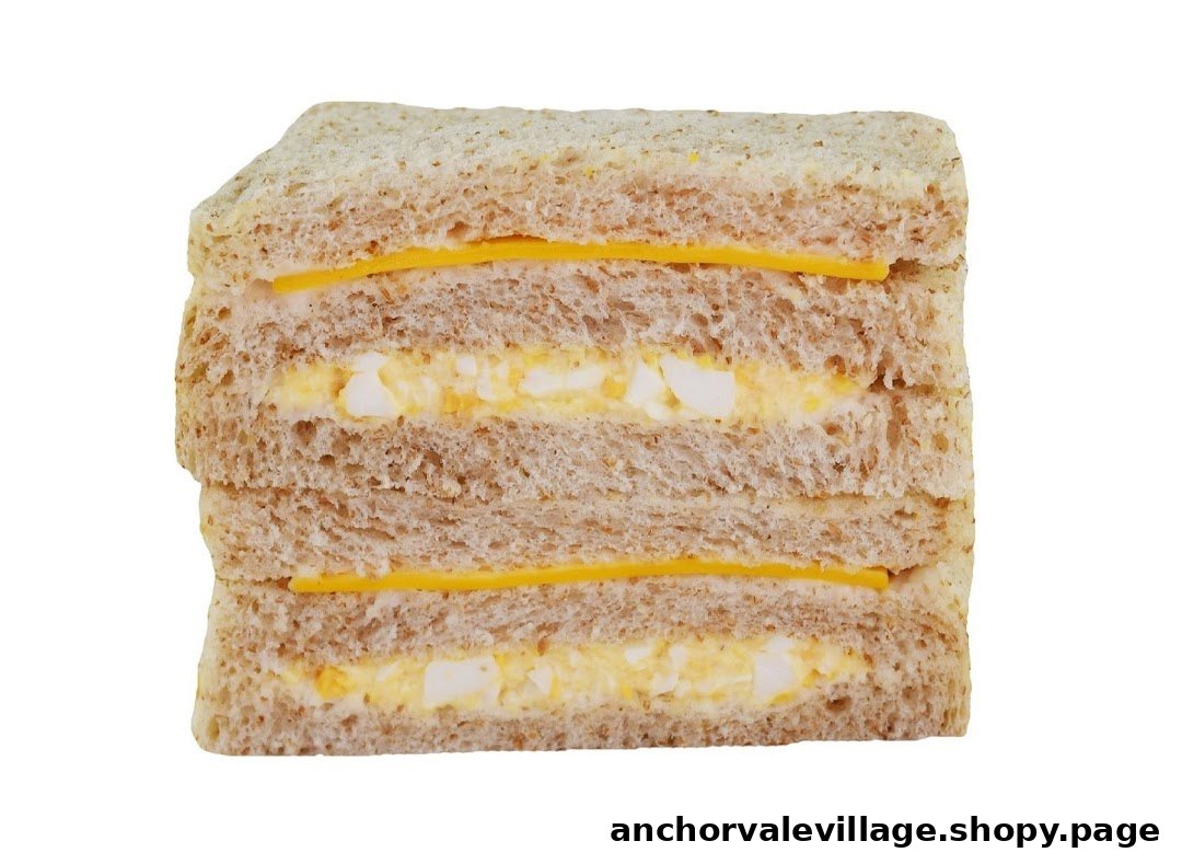 A close-up of a multi-layered sandwich with egg salad and cheese on whole wheat bread.