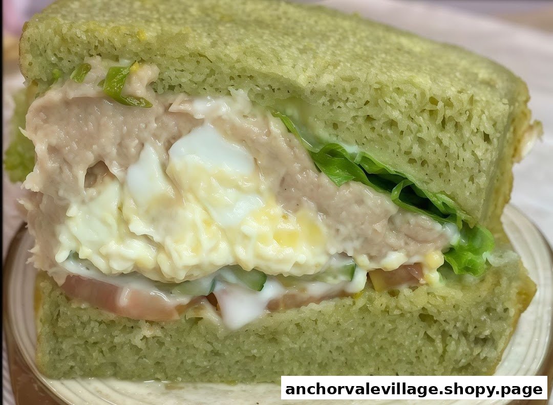 A close-up of a sandwich featuring green bread, tuna, egg, lettuce, and tomato.