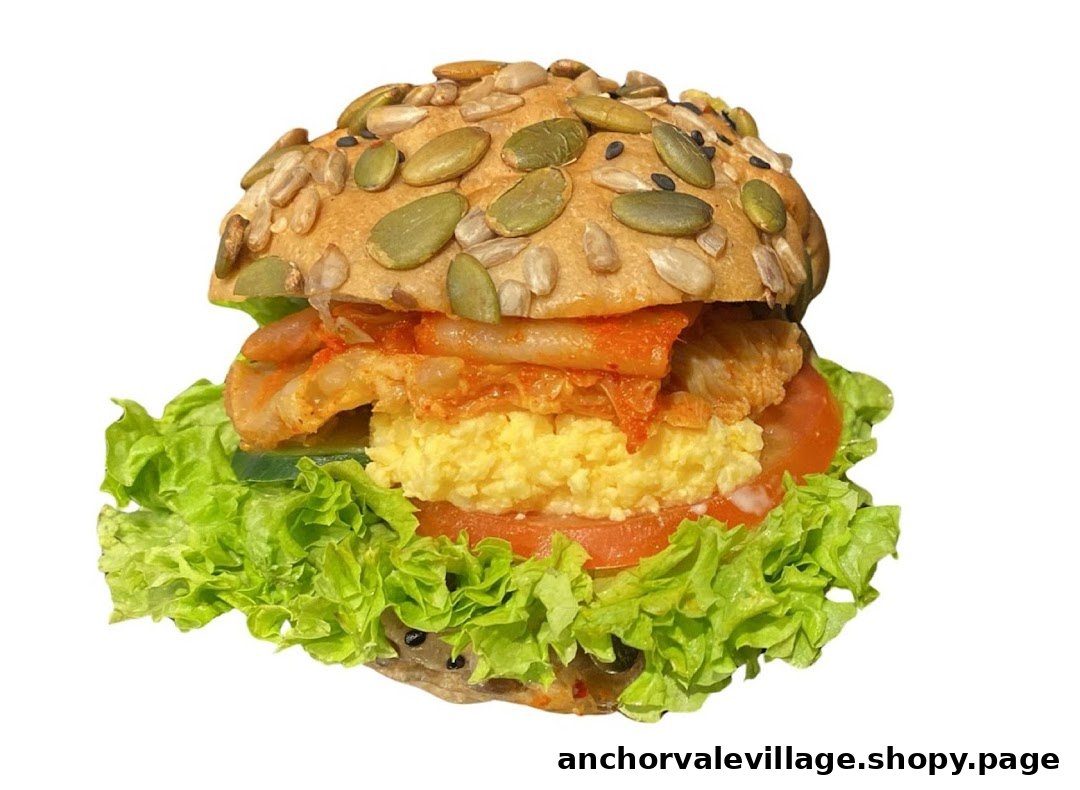 A close-up of a gourmet sandwich with a seed-topped bun, lettuce, tomato, scrambled egg, and kimchi.