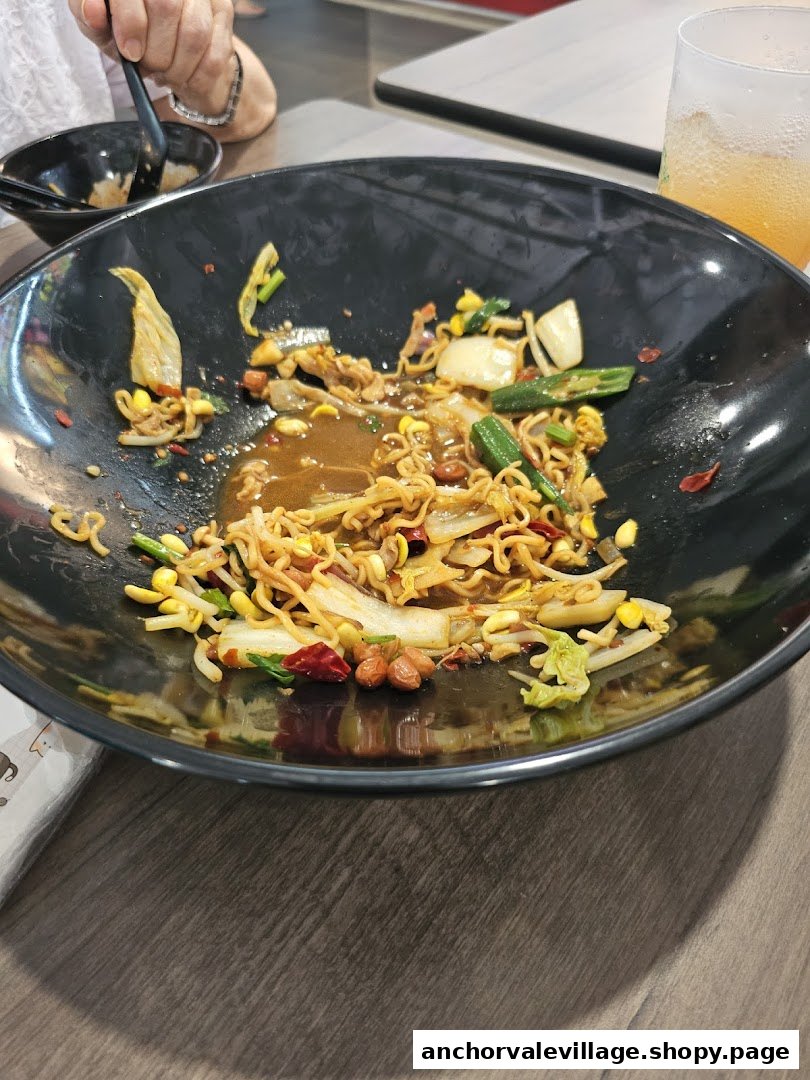 A large black bowl with partially eaten mala hotpot noodles and vegetables on a wooden table.