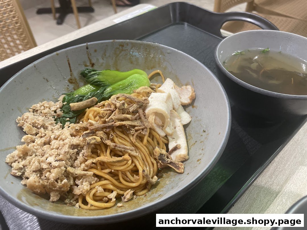 A close-up of Saute Mee noodles with various toppings and a side of clear soup.