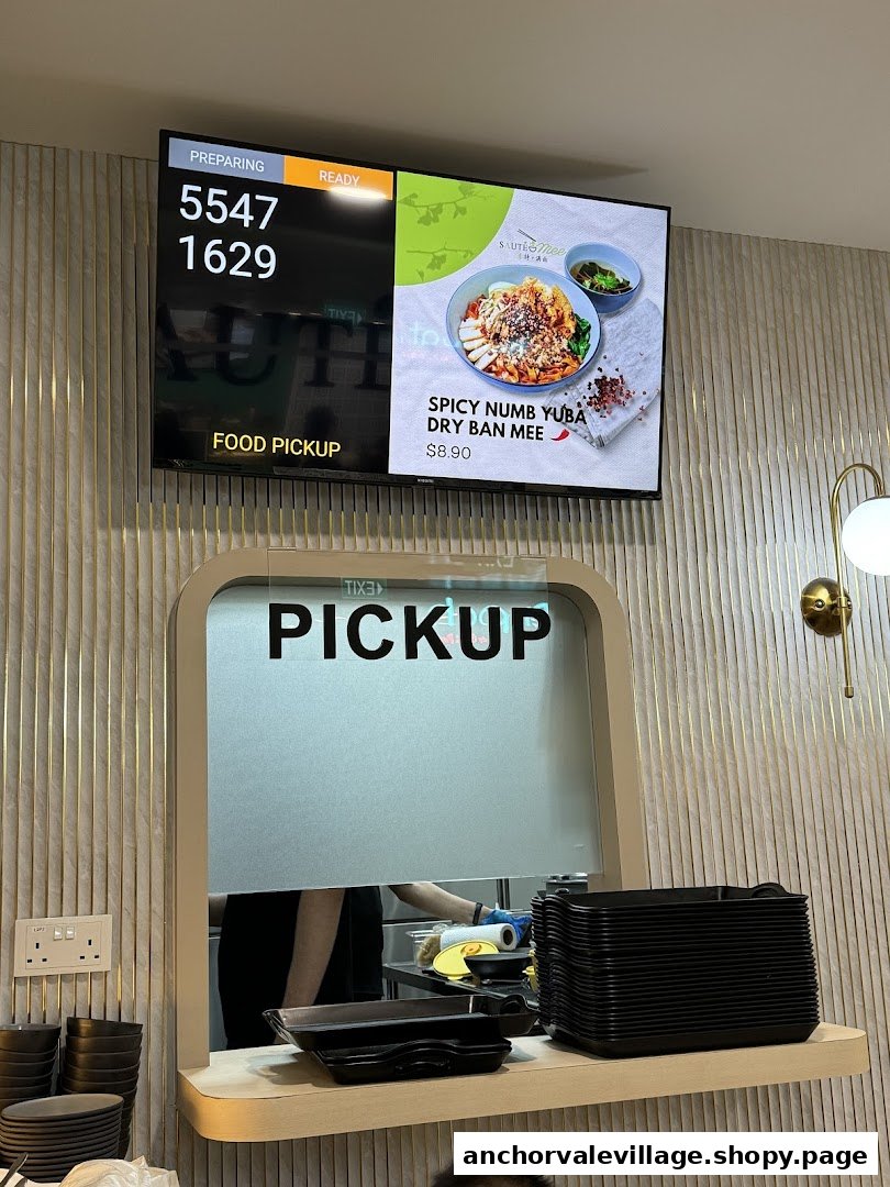 A food pickup counter at Saute Mee, featuring a digital display showing order numbers and a featured dish.