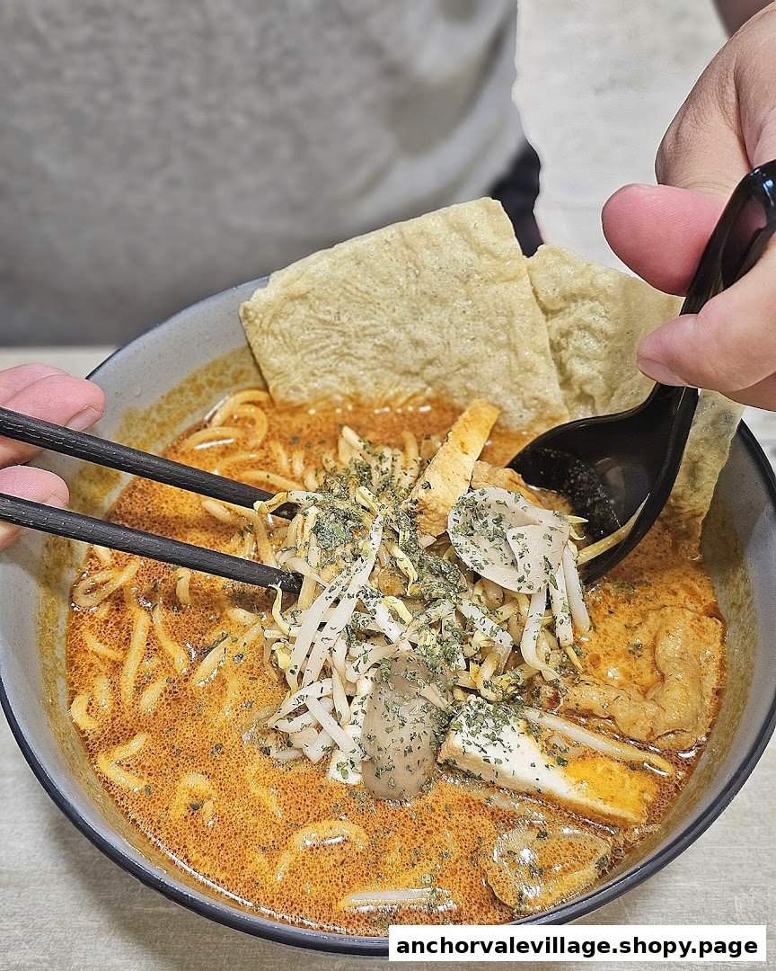 Close-up of a person eating a bowl of vibrant curry noodles with various toppings.