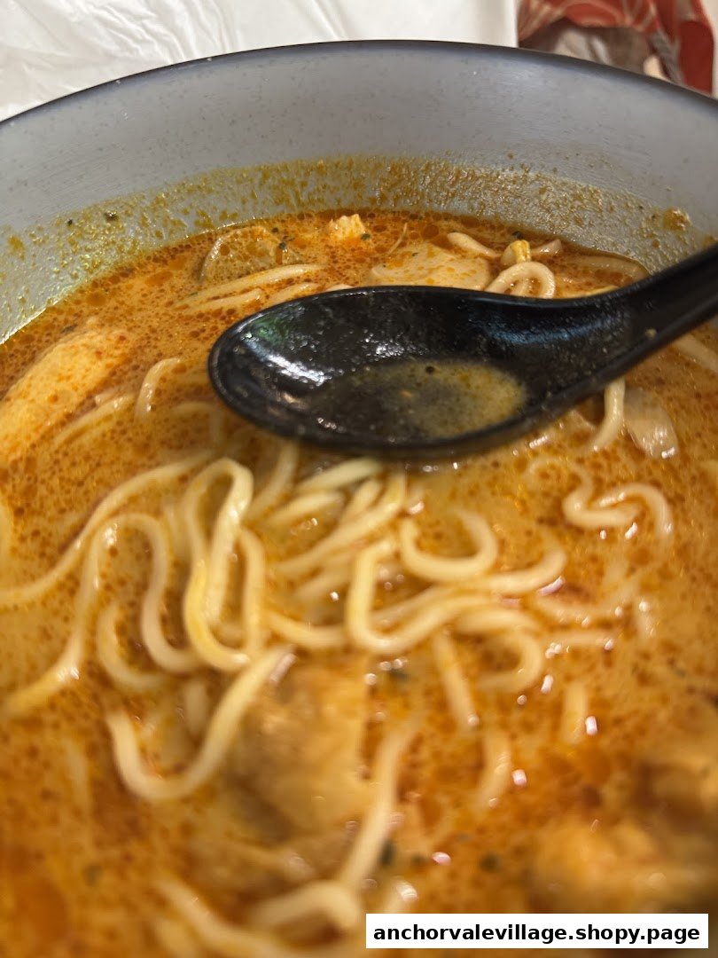 Close-up of a bowl of rich, orange-colored noodles with a black spoon.