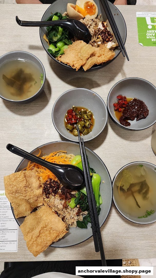 Two bowls of vegan noodles with toppings, side soups, and condiments on a table.
