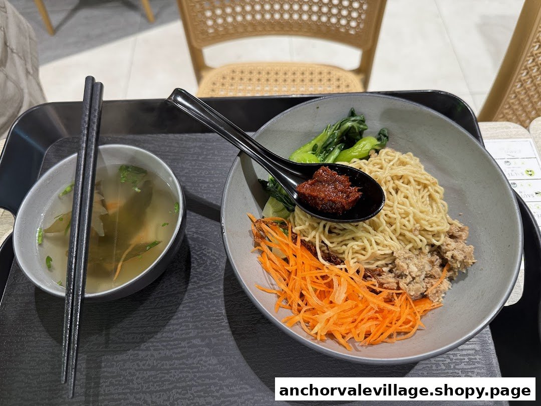 A delicious bowl of vegan noodles with vegetables, minced protein, chili, and a side soup.