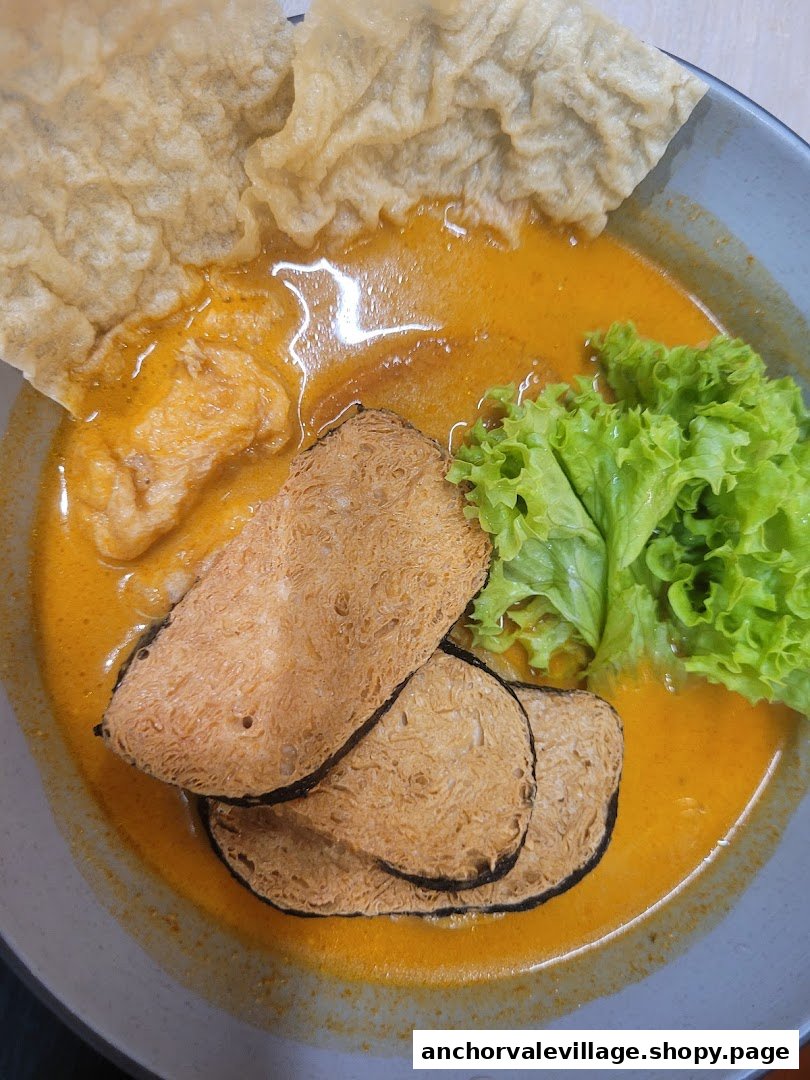 A vibrant bowl of vegan curry noodles with mock meat, lettuce, and crispy crackers.