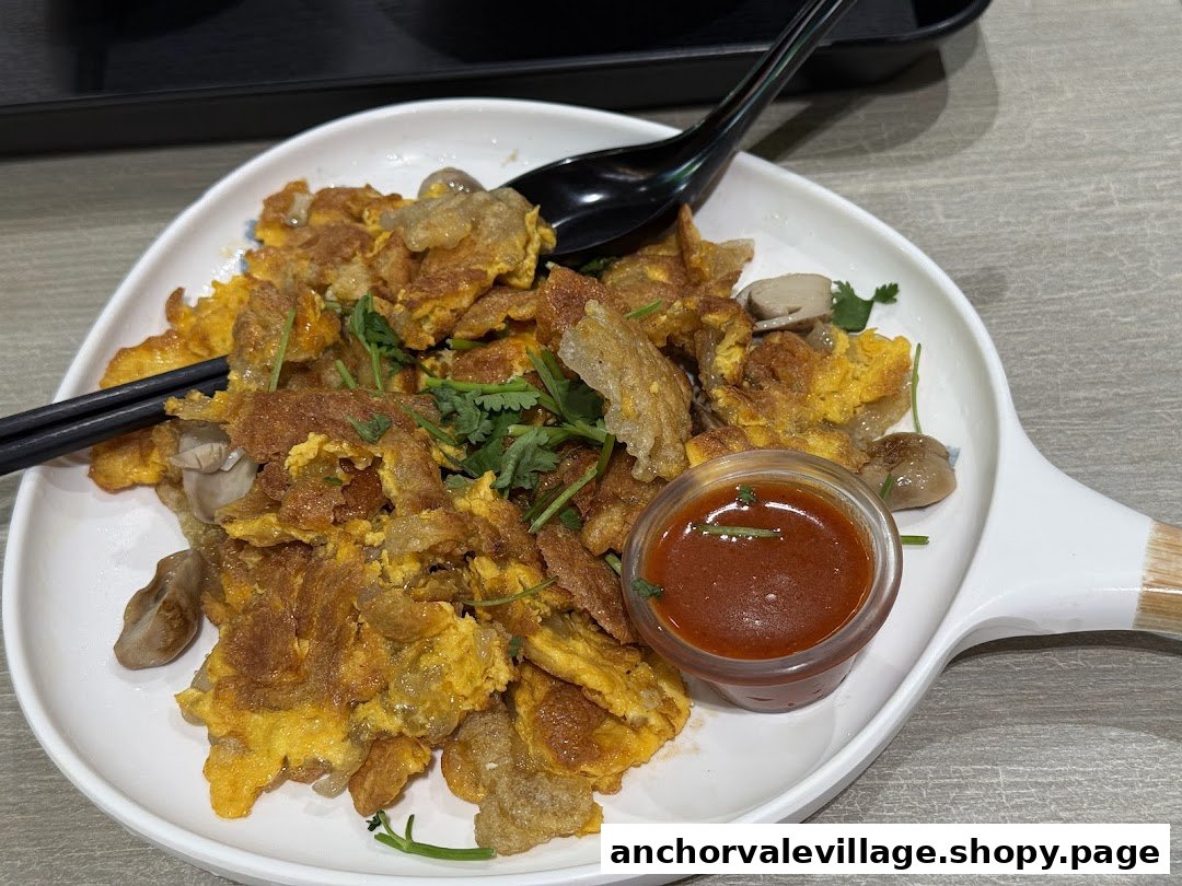 A close-up of a delicious fried omelette dish with mushrooms and a side of chili sauce.