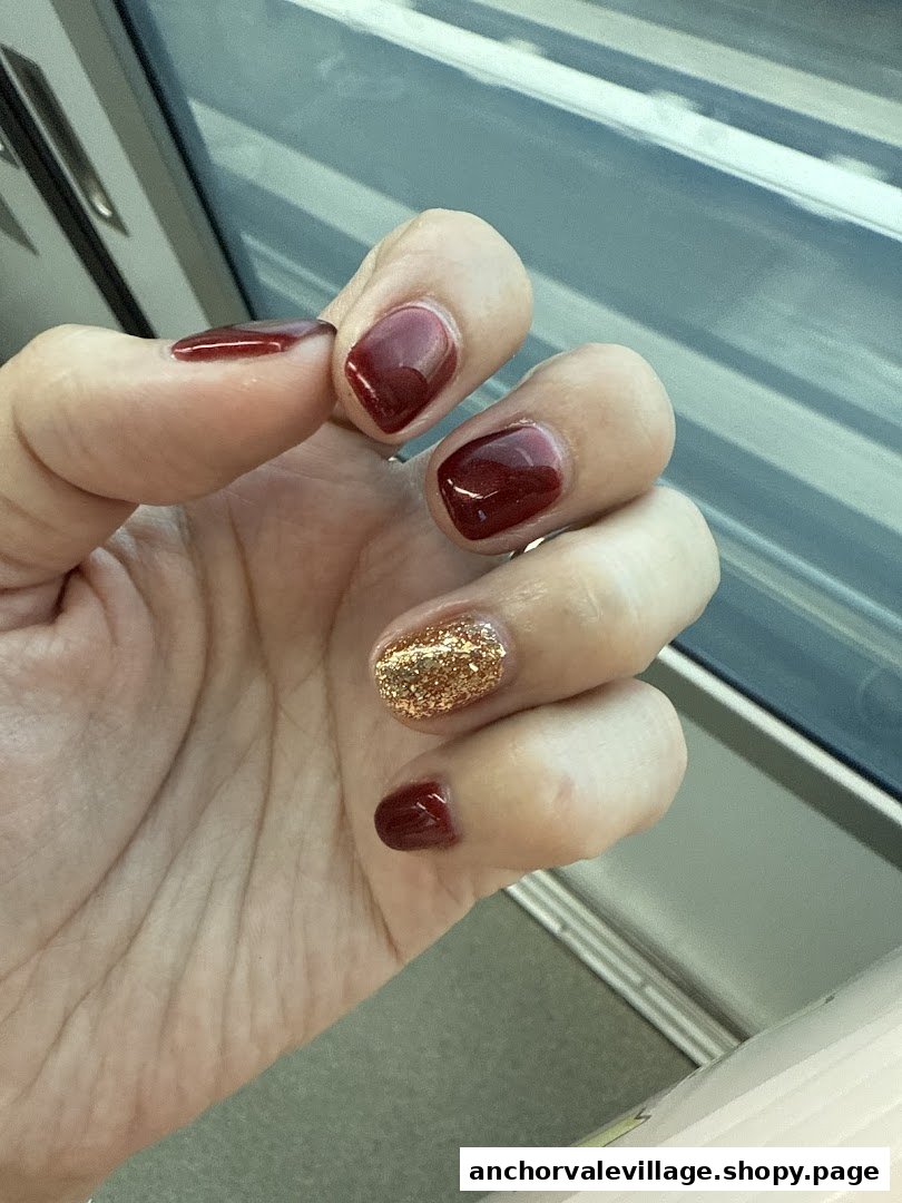 A hand showcasing dark red and sparkling gold glitter nail polish.