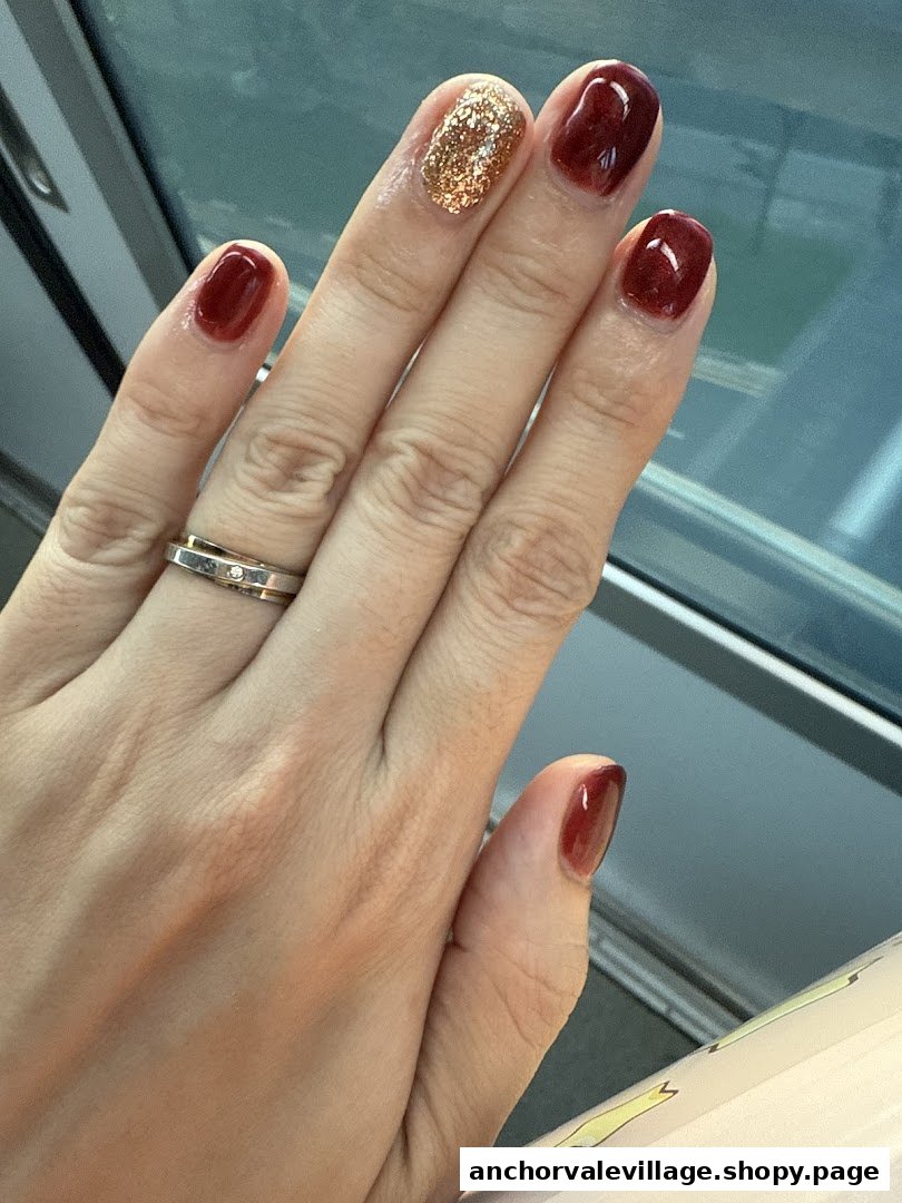 A hand displays beautifully manicured nails with deep red and sparkling gold polish.