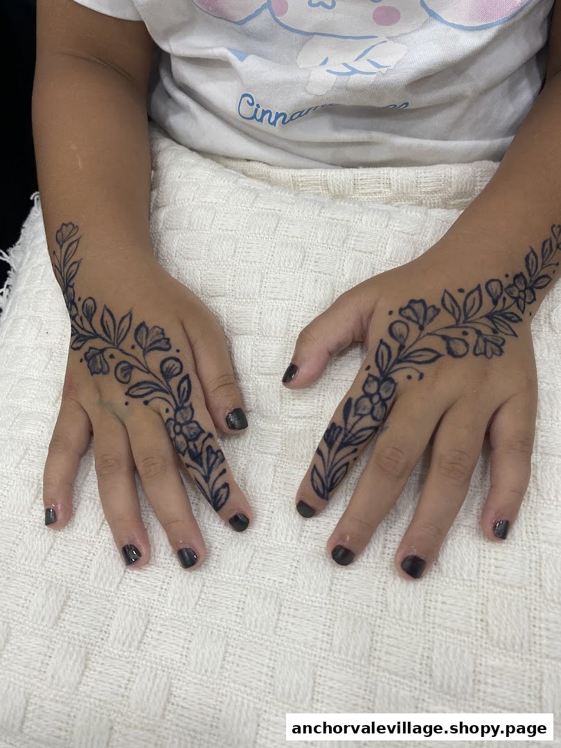 Close-up of hands adorned with intricate floral temporary tattoos and dark nail polish.
