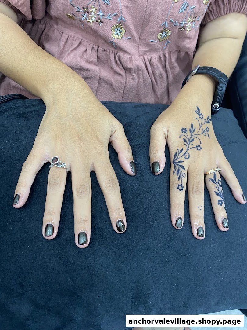 Close-up of hands featuring dark nail polish and an intricate floral henna design.