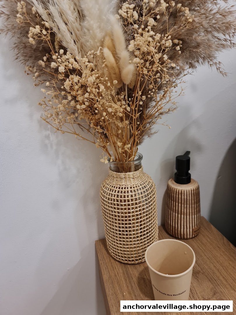 A decorative display featuring dried flowers, a dispenser, and a cup on a wooden surface.