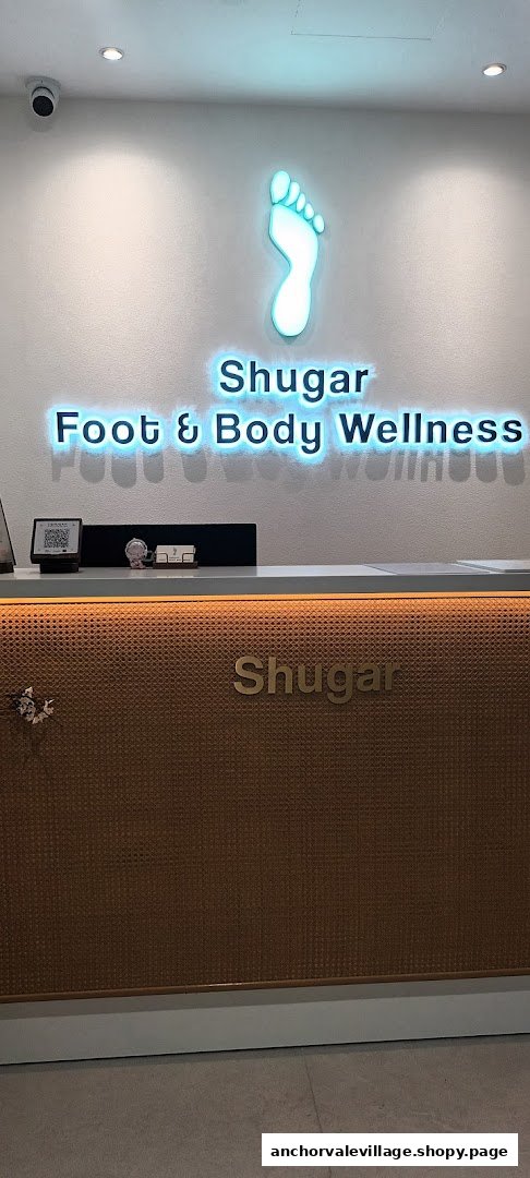 The reception area of Shugar Foot & Body Wellness, featuring a prominent neon logo and counter.