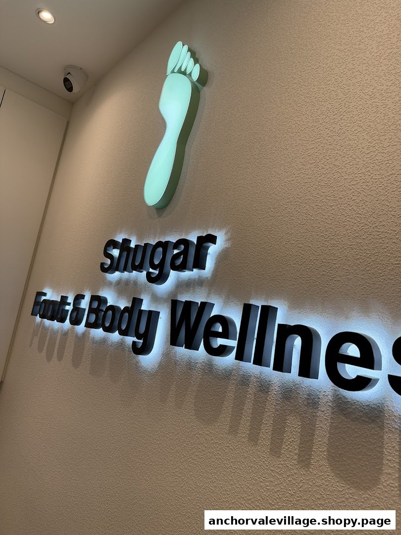 Illuminated Shugar Foot & Body Wellness sign with a foot logo on a textured wall.