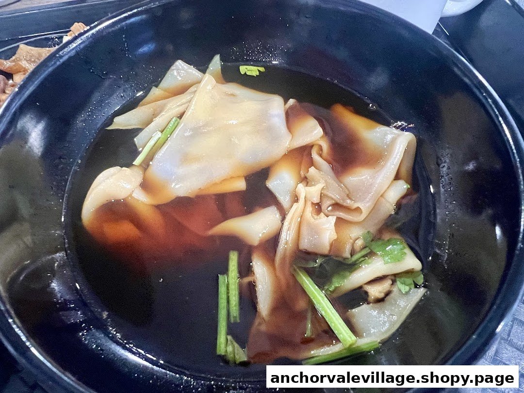 A close-up of a bowl of Kway Chap featuring flat rice sheets in a rich, dark broth.