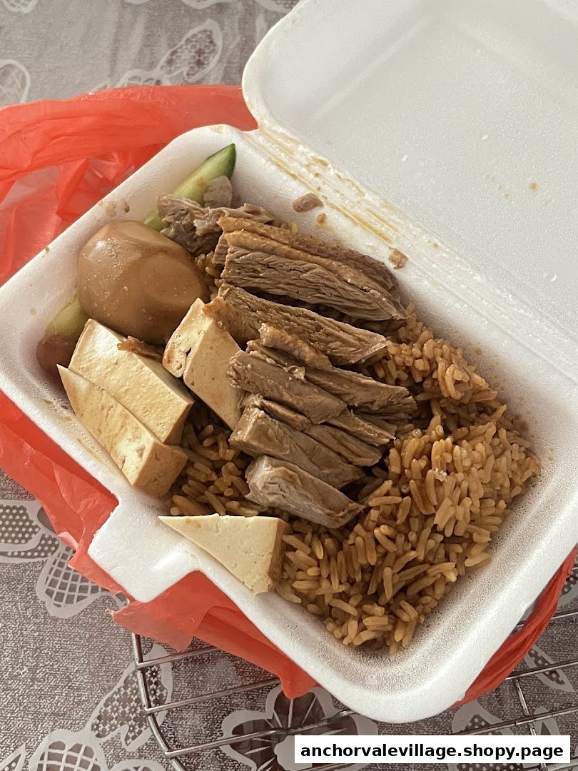 A takeaway box of braised duck rice with tofu, egg, and cucumber.