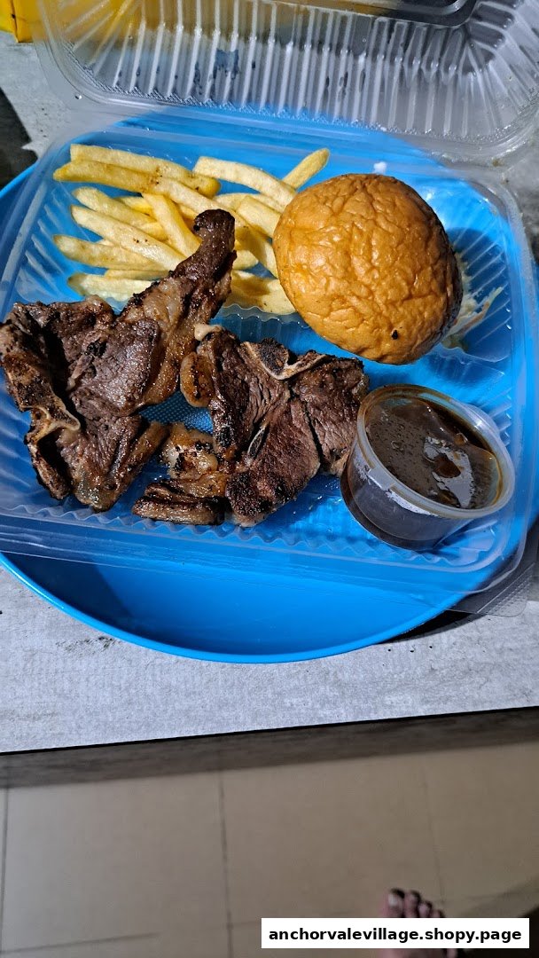 A takeaway meal featuring grilled lamb chops, golden fries, a bun, and a side of sauce in a blue container.