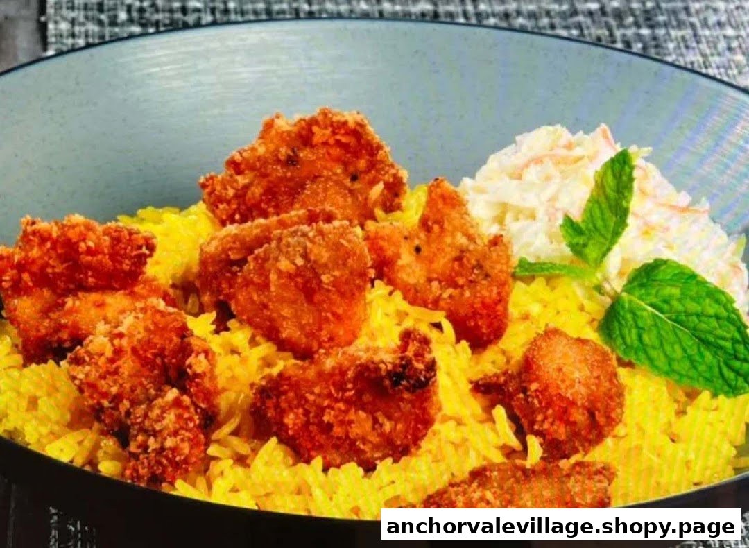A close-up of crispy fried chicken pieces served on vibrant yellow rice with coleslaw and fresh mint.