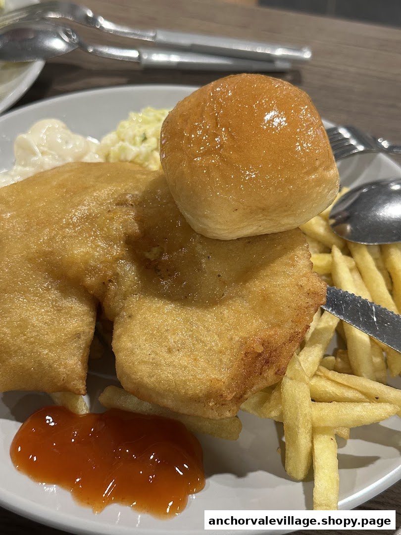 A close-up of a golden-fried chicken or fish fillet with fries, a bun, coleslaw, and sauces.