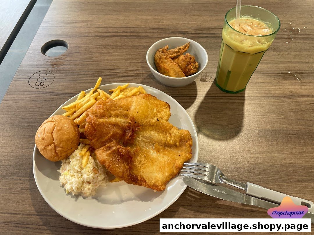 A plate of golden-fried fish and chips with coleslaw, a bun, chicken wings, and a drink on a wooden table.