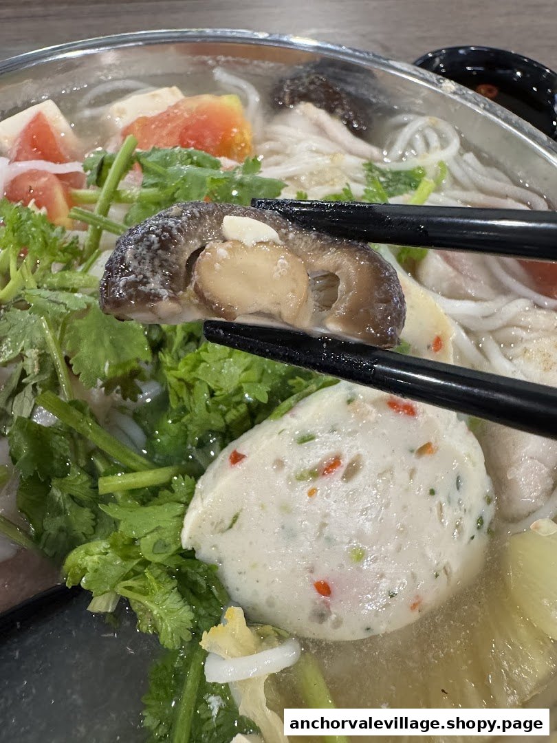 Close-up of a delicious fish soup bowl with various ingredients, including a mushroom held by chopsticks.