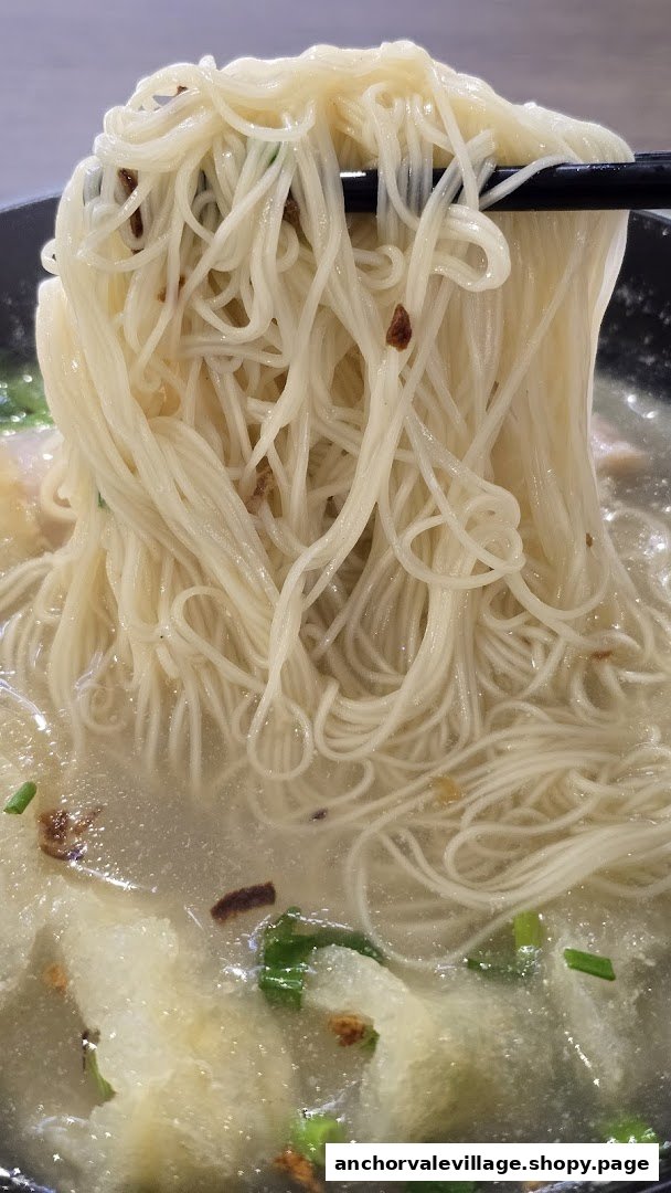 Chopsticks lift a generous portion of white noodles from a bowl of fish soup.
