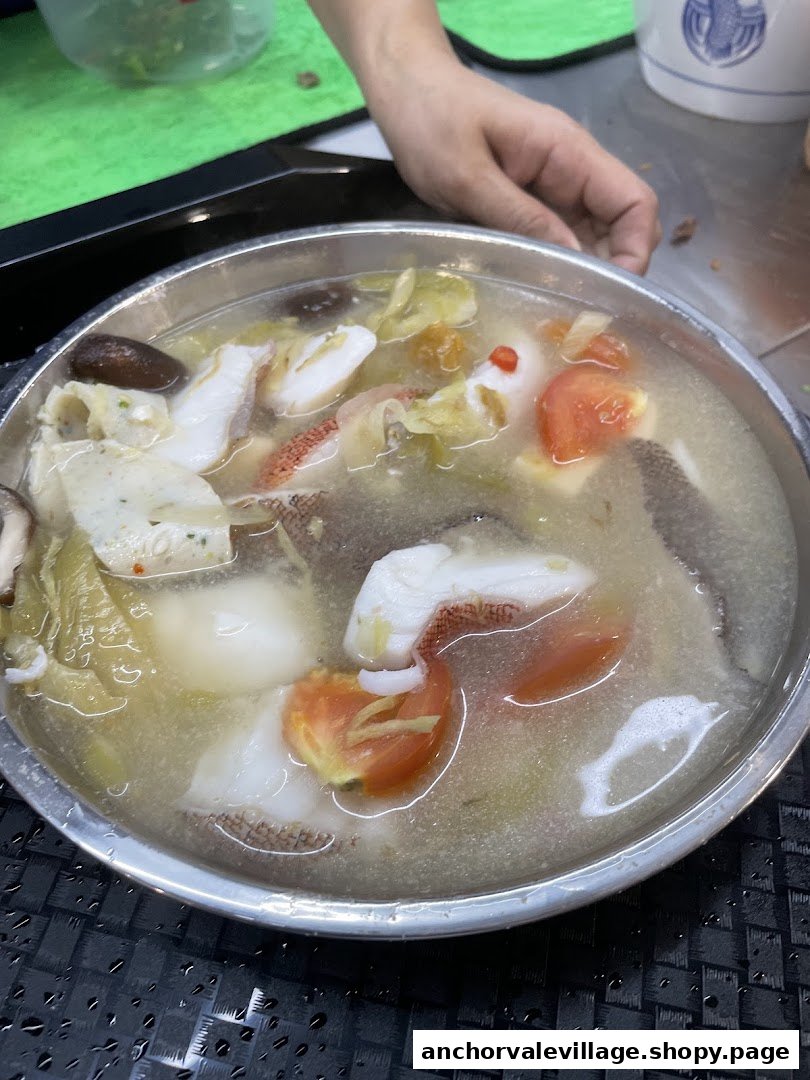 A close-up of a steaming bowl of fish soup with fish slices, tomatoes, and vegetables.