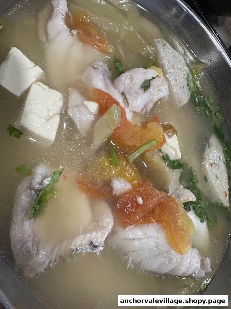A close-up of a steaming bowl of fish soup with fresh fish slices, tofu, and vegetables.