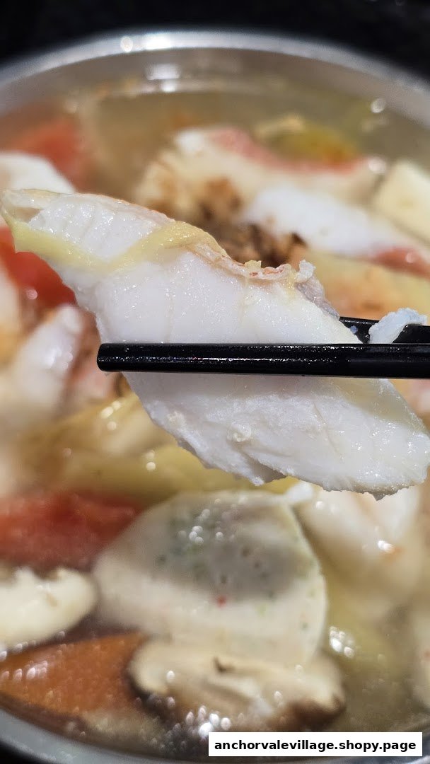 A close-up of a fresh fish slice held by chopsticks over a bowl of delicious fish soup.