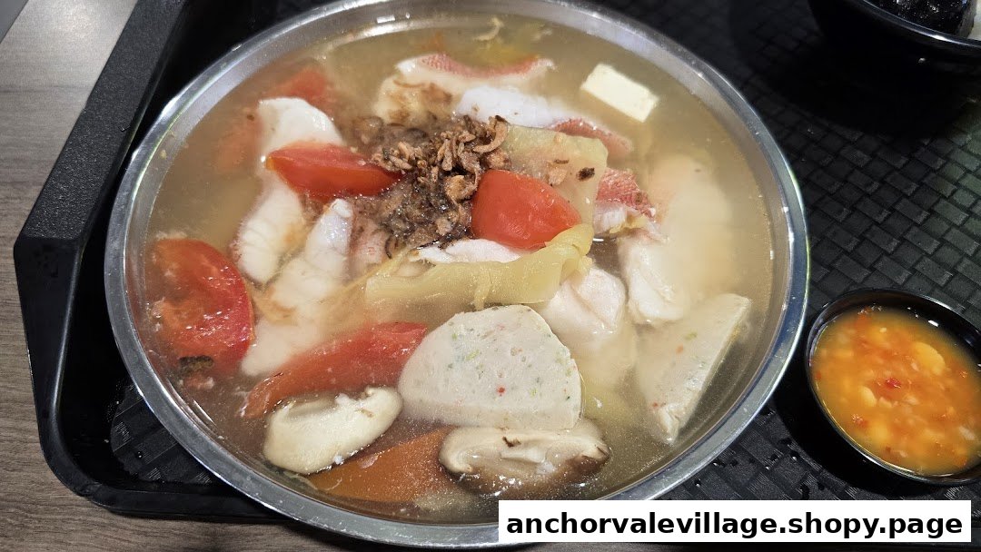 A close-up of a steaming bowl of fish soup with fish slices, tomatoes, and other ingredients.