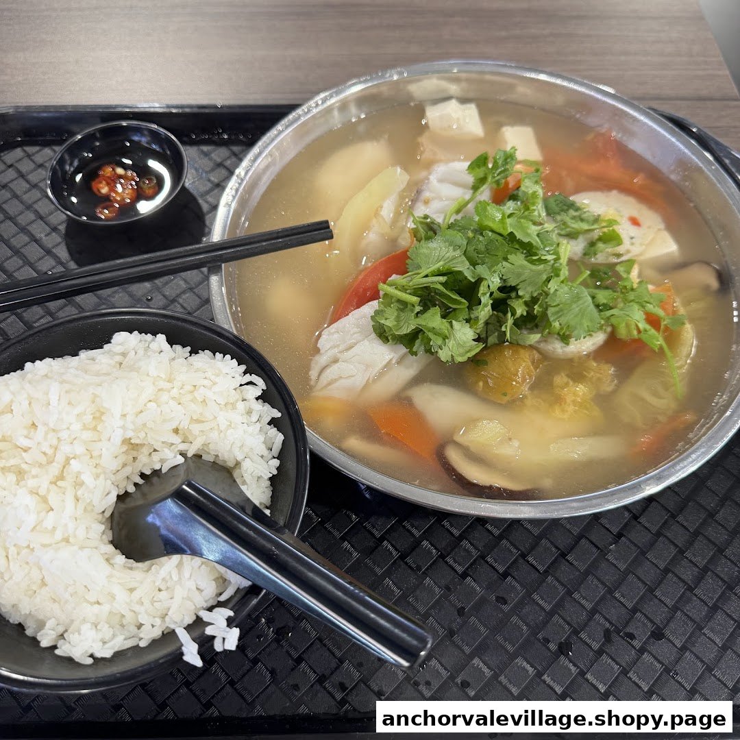 A hearty bowl of fish soup with fresh ingredients, served with a side of white rice and chili.