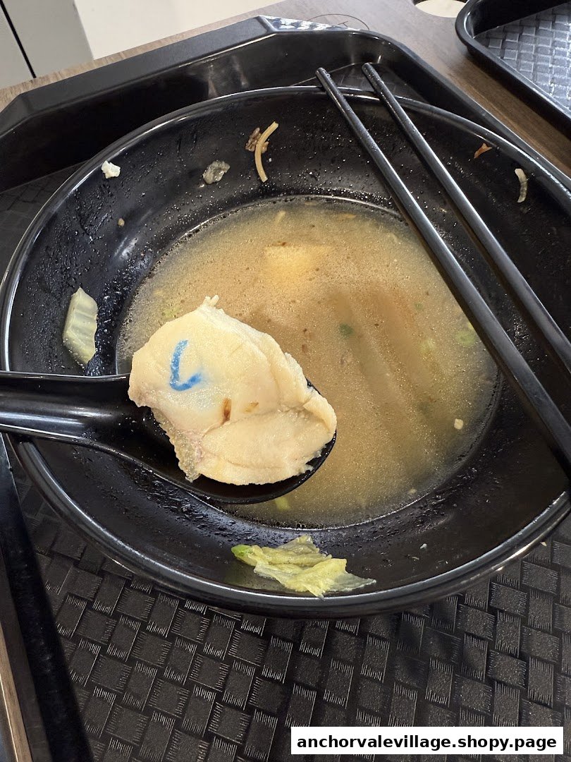 A close-up of a nearly finished bowl of fish soup with a piece of fish on a spoon.