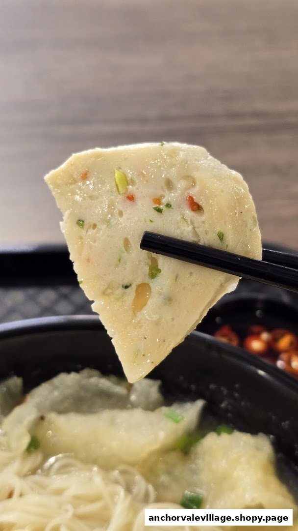 A close-up of a delicious fish cake held by chopsticks, part of a noodle dish from Soon Lee Fish Soup.