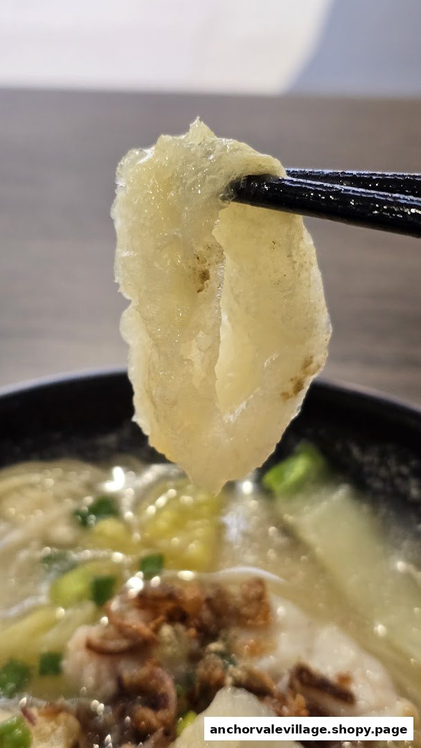 Chopsticks holding a piece of fish maw or similar ingredient from a bowl of fish soup.