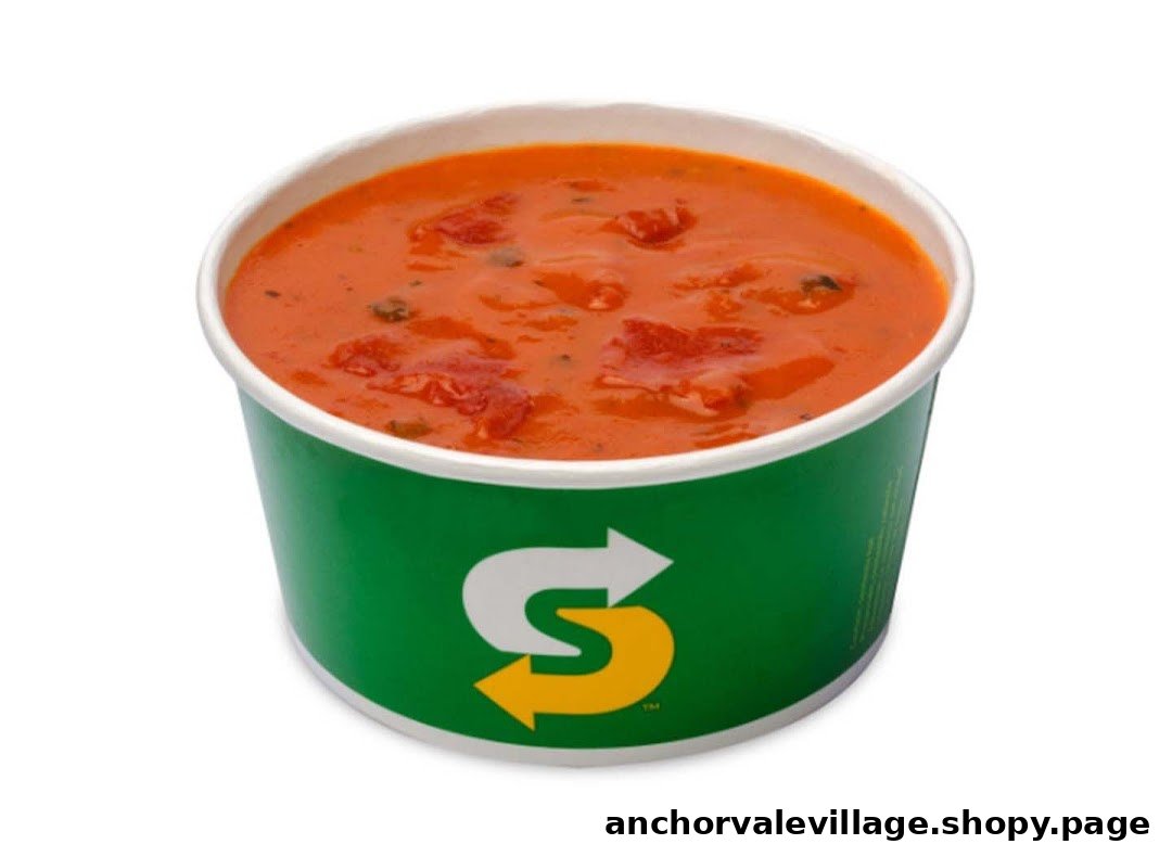 A vibrant orange tomato-based soup in a green Subway branded cup.