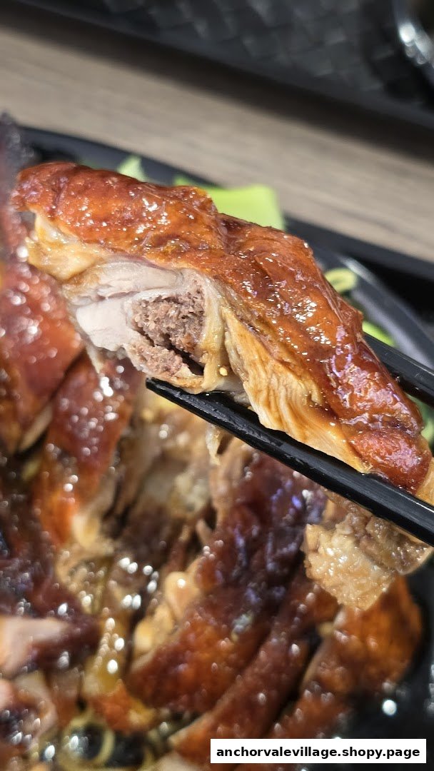 A close-up of a succulent piece of roasted meat, likely duck or chicken, held by chopsticks, showcasing its tender interior.