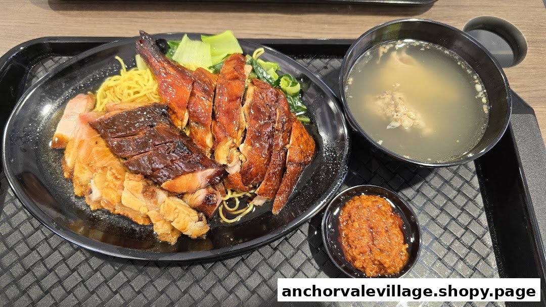 A delicious platter of roasted duck, char siu, and crispy pork belly with noodles, soup, and chili.